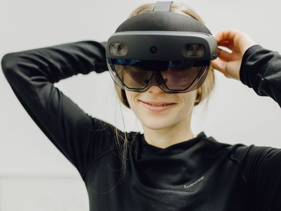Foto von Frau die lächelnd mit großer VR-Brille in Kamera blickt 
