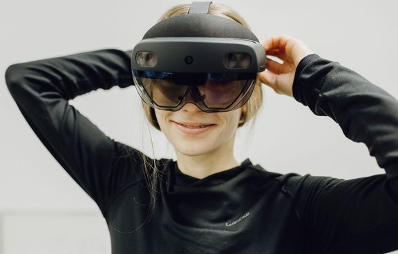 Foto von Frau die lächelnd mit großer VR-Brille in Kamera blickt 

