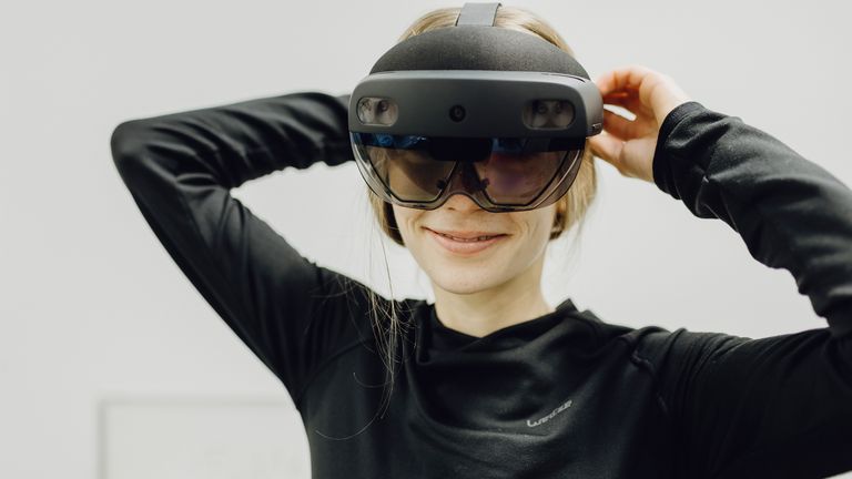 Foto von Frau die lächelnd mit großer VR-Brille in Kamera blickt 
