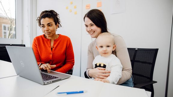 Mutter mit Kind blickt auf Laptop während einer Beratung
