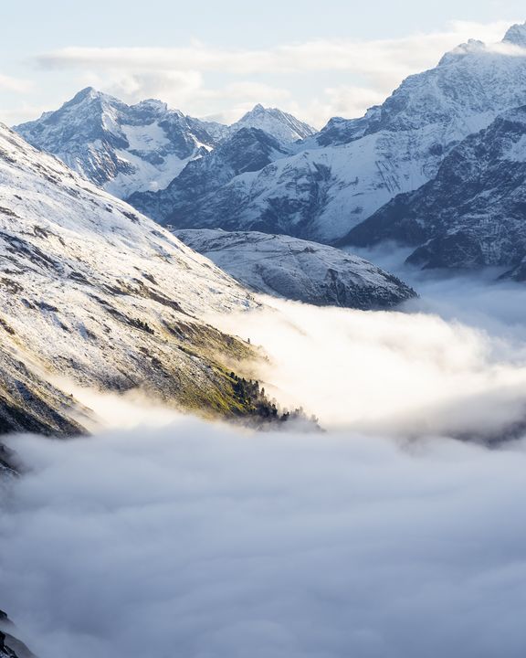 Berglandschaft mit schneebedeckten Gipfeln und einem Tal, das von Wolken bedeckt ist
