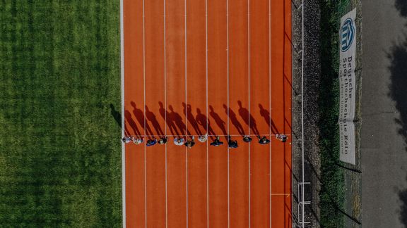 Ansicht von oben auf einige Studenten mit großen Schatten die an einer Linie auf der Laufbahn der Deutschen Sporthochschule bereit stehen
