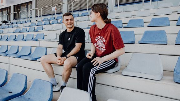 Mann und Frau sitzen im Stadion und unterhalten sich
