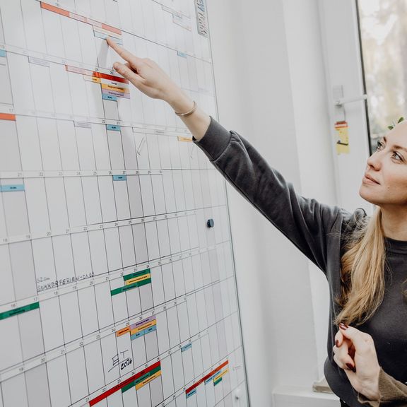 Foto von zwei Frauen die auf Terminkalender an Whiteboard zeigen
