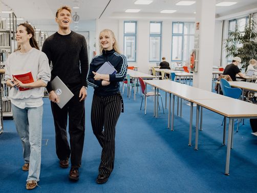 Drei Studierende laufen durch die Bibliothek der Deutschen Sporthochschule
