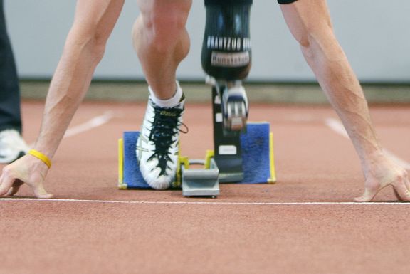 Ein/eine Läufer*in mit Beintprothese in Startposition im  Startblock. Man sieht nur das Bein und die Prothese sowie beide Arme. Oberkörper und Kopf sind nicht erkennbar.
