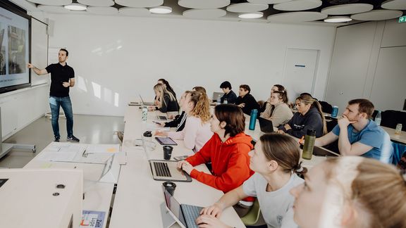 Studierende werden im Seminarraum vom Dozierenden unterrichtet
