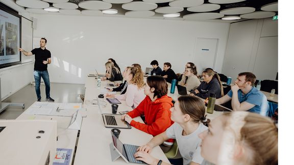Studierende werden im Seminarraum vom Dozierenden unterrichtet
