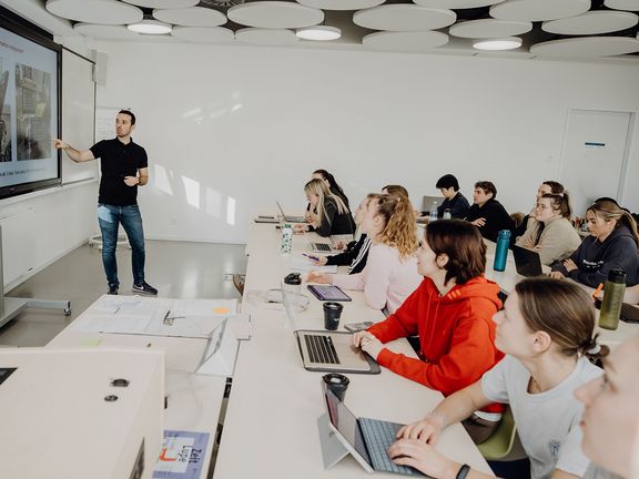 Studierende werden im Seminarraum vom Dozierenden unterrichtet
