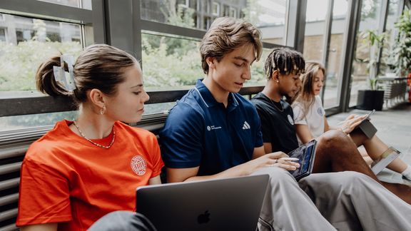 Drei Studierende arbeiten mit Laptops im Foyer der Deutschen Sporthochschule
