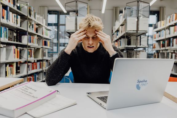Student stützt sich frustriert mit seinen Händen auf dem Tisch ab in der Bibliothek 
