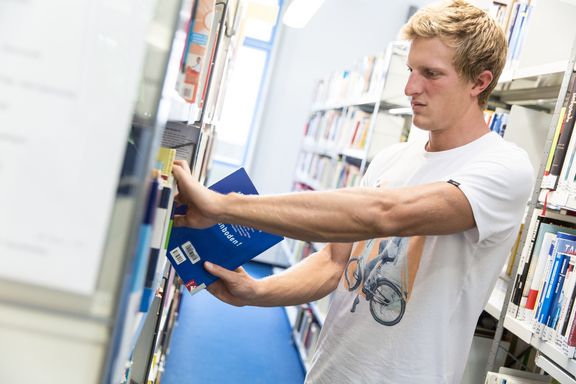 Ein Student nimmt ein Buch aus einem Regal in der Bibliothek
