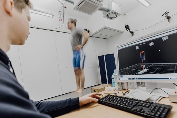 Foto von Mann der senkrecht nach oben springt während ein Forscher die Messung in 3D-Umgebung auf seinem PC betrachtet
