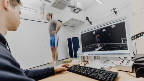 Foto von Mann der senkrecht nach oben springt während ein Forscher die Messung in 3D-Umgebung auf seinem PC betrachtet
