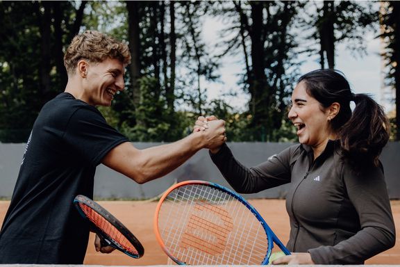Foto von zwei Personen die sich mit Tennisschlägern in der Hand abklatschen
