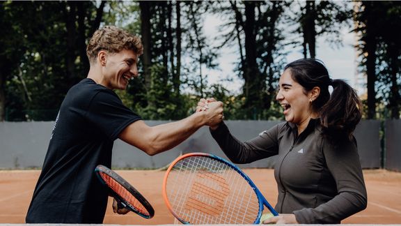 Foto von zwei Personen die sich mit Tennisschlägern in der Hand abklatschen
