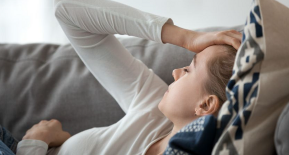 Person liegt auf Sofa und hält sich den Kopf
