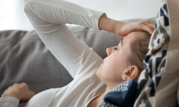 Person liegt auf dem Sofa und hält sich den Kopf
