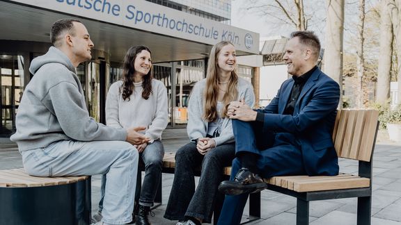 Gespräch zwischen drei Studierenden und dem Rektor der Sporthochschule vor dem Haupteingang
