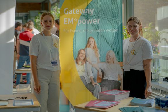 Zwei Frauen stehen an einem Stand bei einem Event
