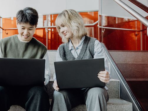 Zwei Studierende sitzen mit Laptops im Treppenhaus
