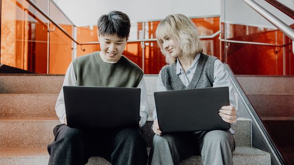 Zwei Studierende sitzen mit Laptops im Treppenhaus
