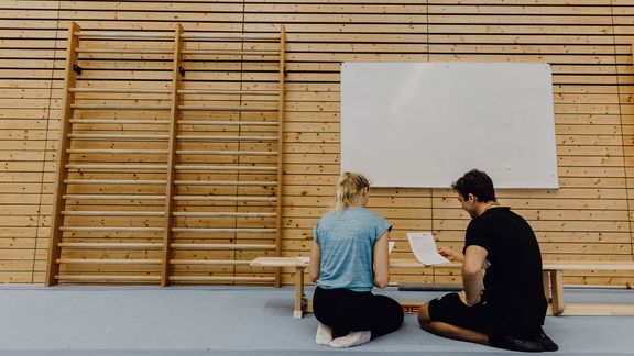 Studierende betrachten Formulare in der Turnhalle

