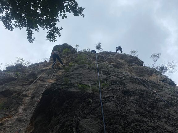 Drei Personen seilen sich an einer steilen Felswand ab, Blick von unten nach oben
