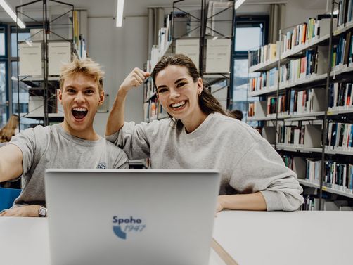 Zwei Studierende freuen sich mit geballter Faust in der Bibliothek
