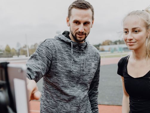 Foto von zwei Personen die auf ein Tablet auf einem Sportplatz blicken
