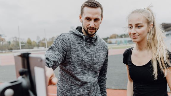 Foto von zwei Personen die auf ein Tablet auf einem Sportplatz blicken
