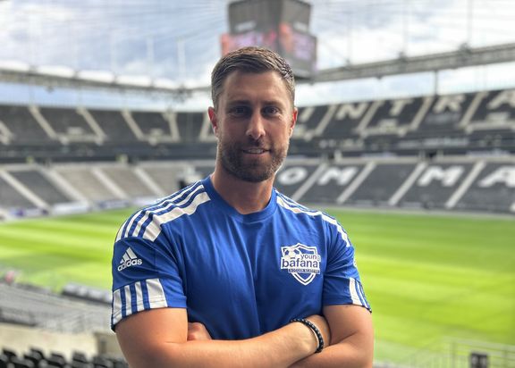 Porträtfoto von Sebastian Stahl. Er steht in einem blauen Sportshirt in einem Stadion. Er hat seine Arme vor dem Körper verschränkt.
