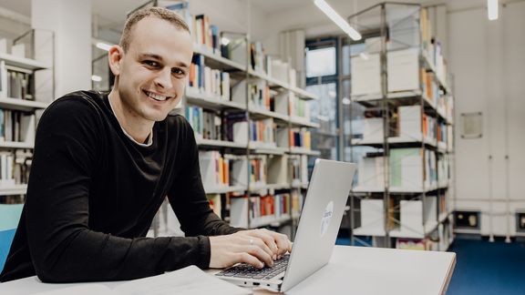 Student sitzt mit Laptop in der Bibliothek der Deutschen Sporthochschule
