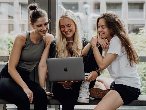 Dire Studierende sitzen mit einem Laptop im Foyer der Deutschen Sporthochschule

