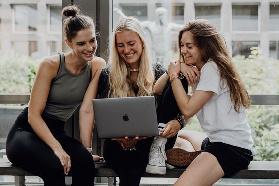 Dire Studierende sitzen mit einem Laptop im Foyer der Deutschen Sporthochschule
