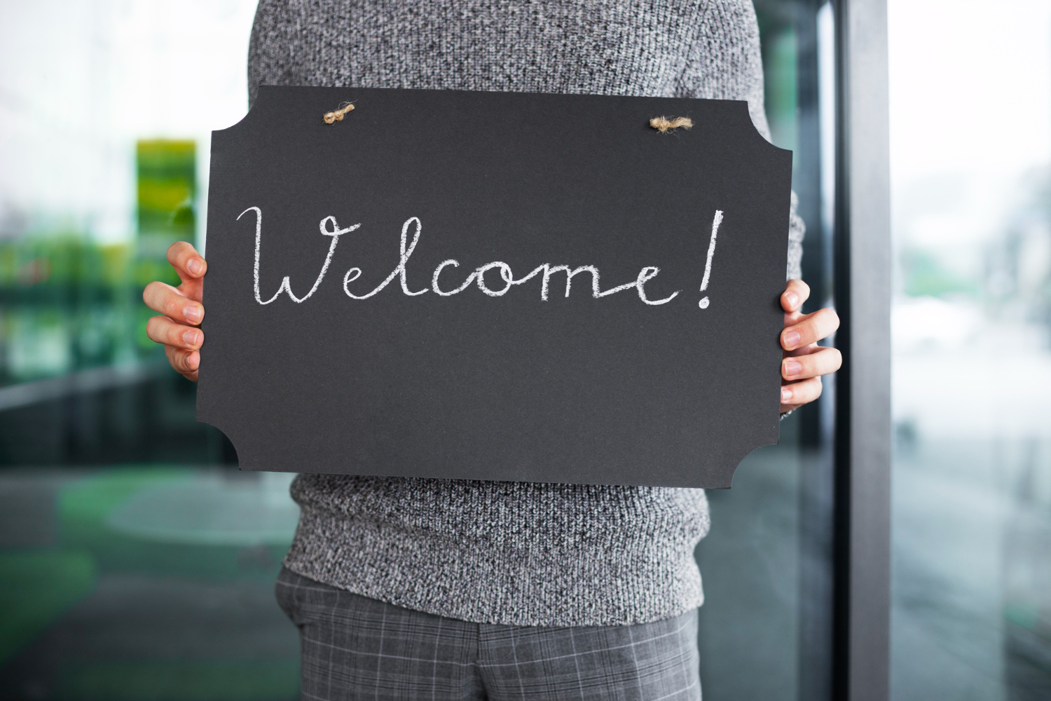 Ein Mann hält eine Tafel mit der Beschriftung Welcome in die Kamera