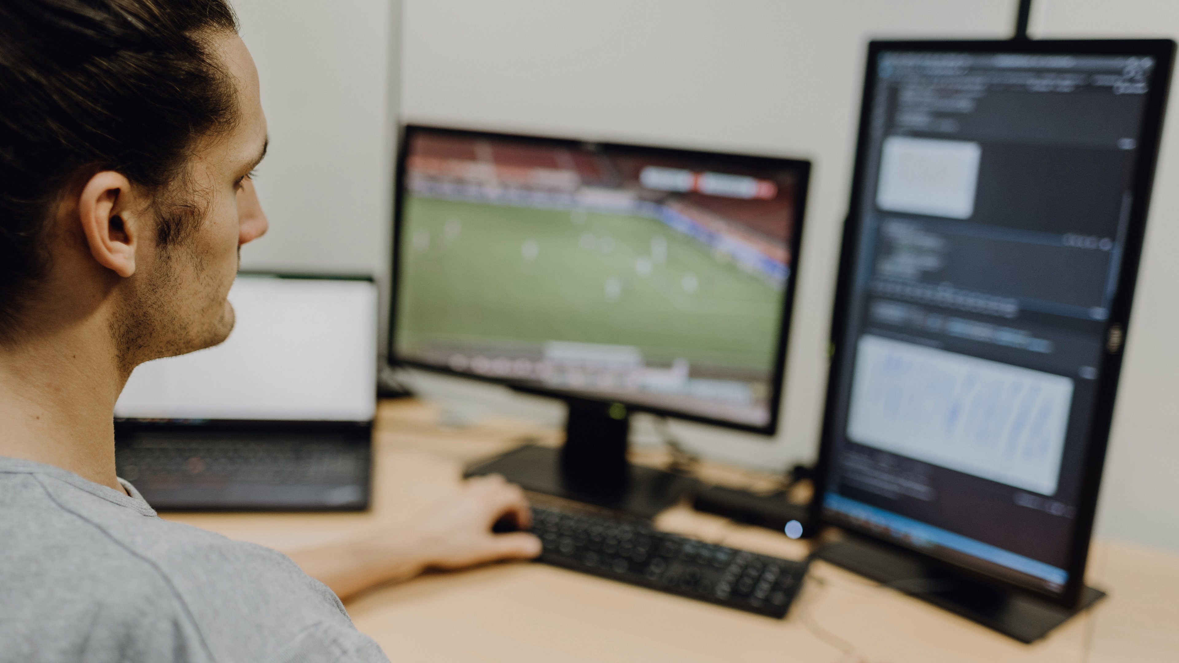 Foto von Mann der auf auf Programmiercode neben laufendem Fußballspiel blickt
