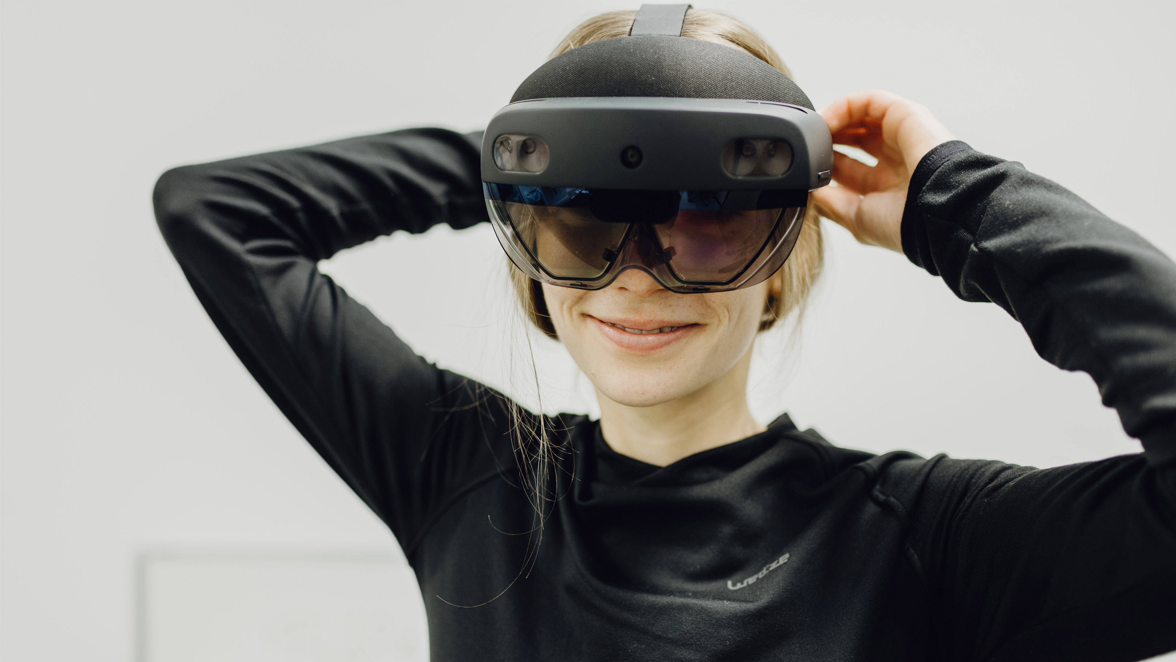 Foto von Frau die lächelnd mit großer VR-Brille in Kamera blickt 
