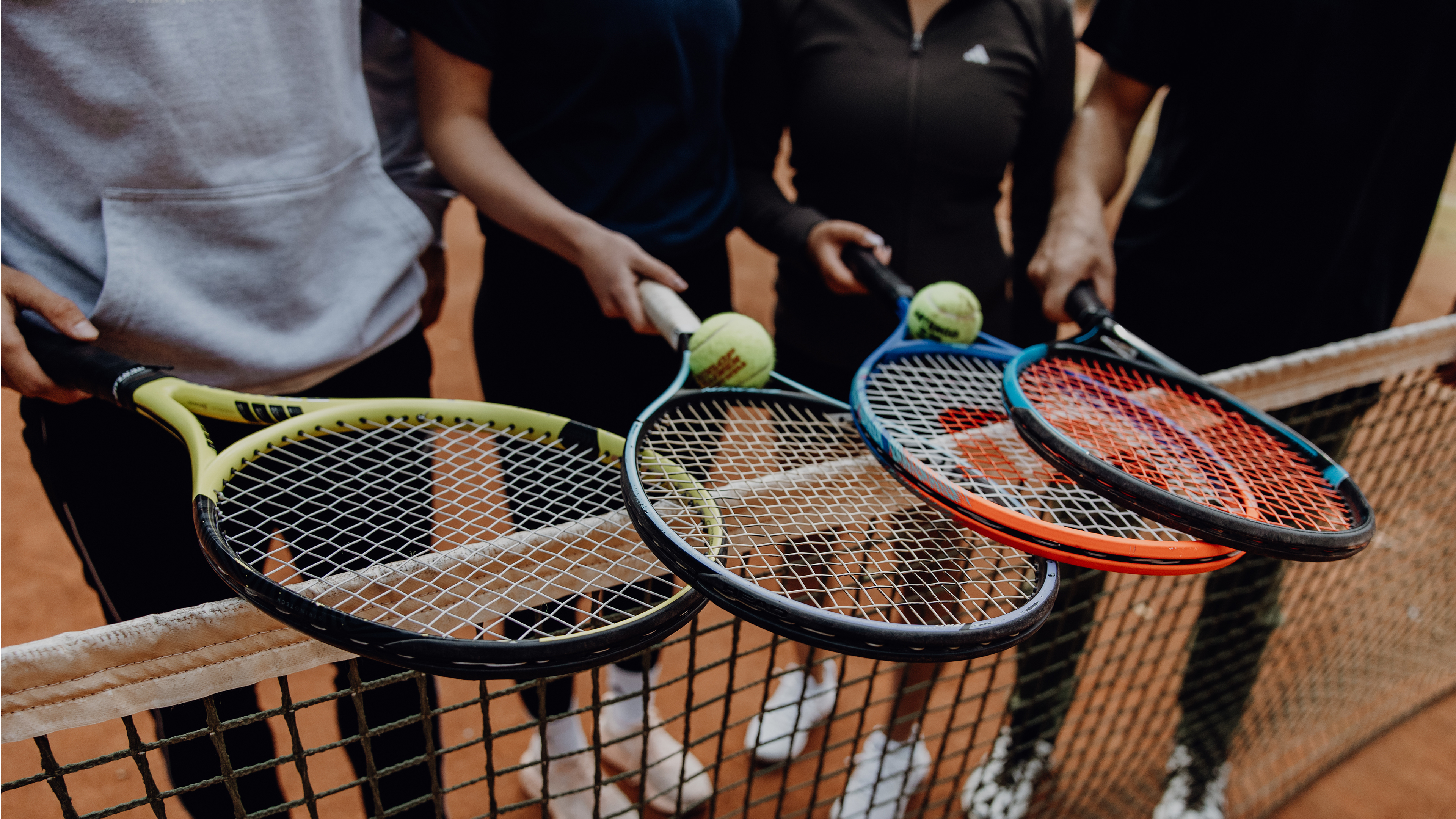 Foto von vier Tennisschlägern die über das Tennisnetz gehalten werden
