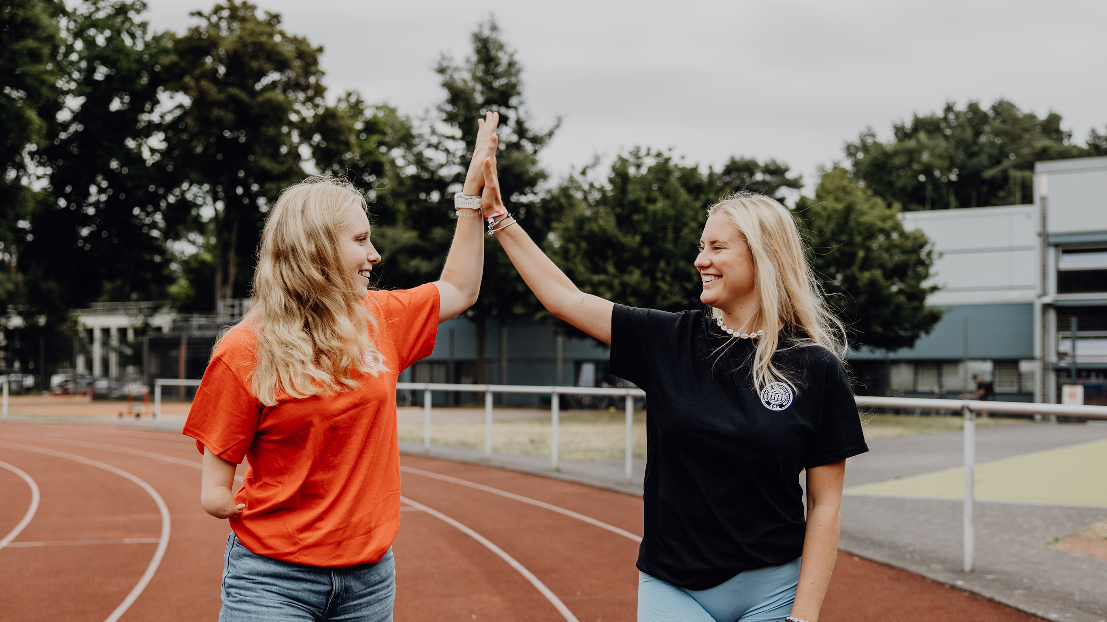 Zwei Studentinnen geben sich auf einer Laufbahn im Freien ein High-Five.
