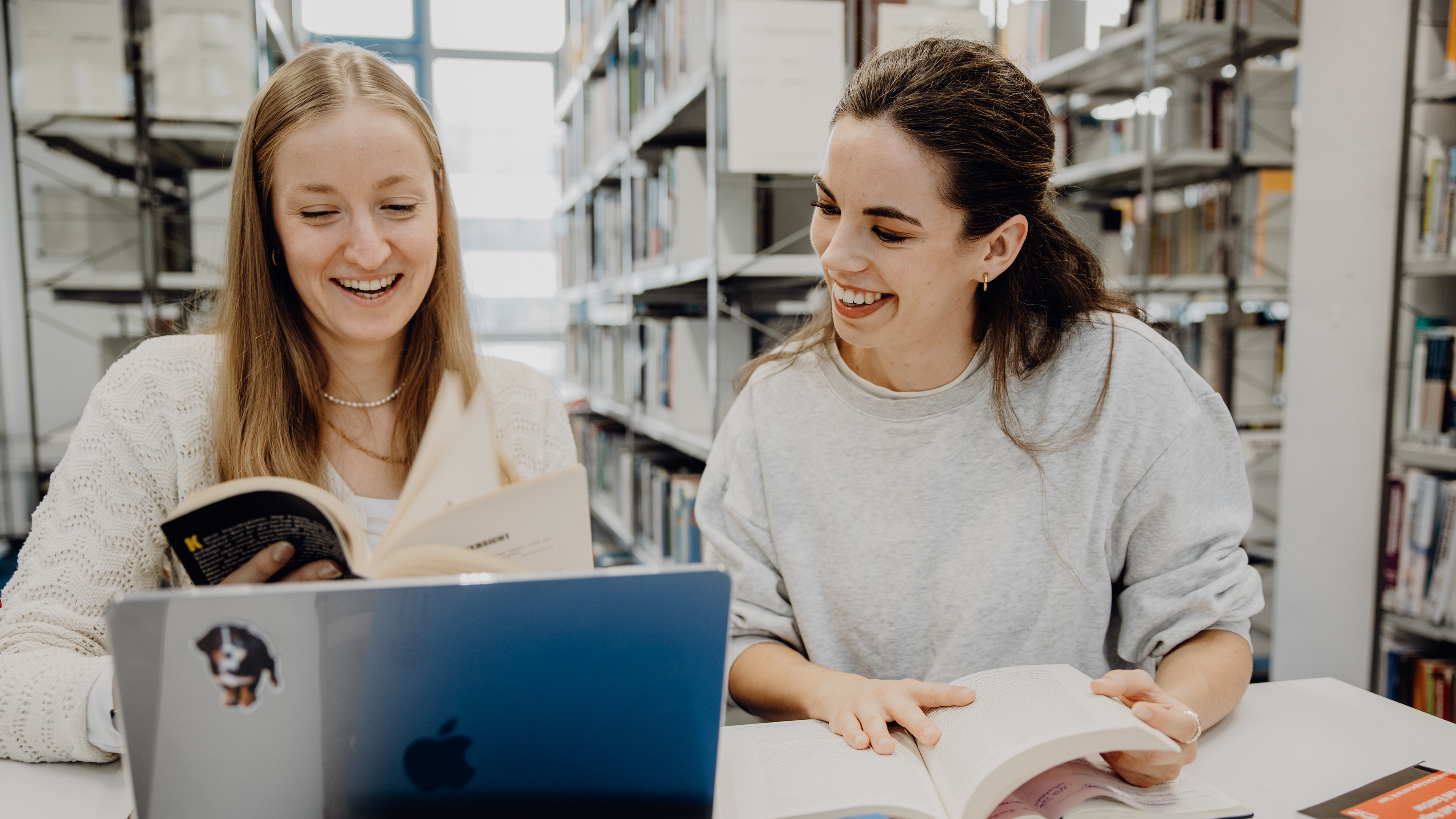 Zwei Studentinnen blättern durch ein Buch in der Bibliothek der Deutschen Sporthochschule
