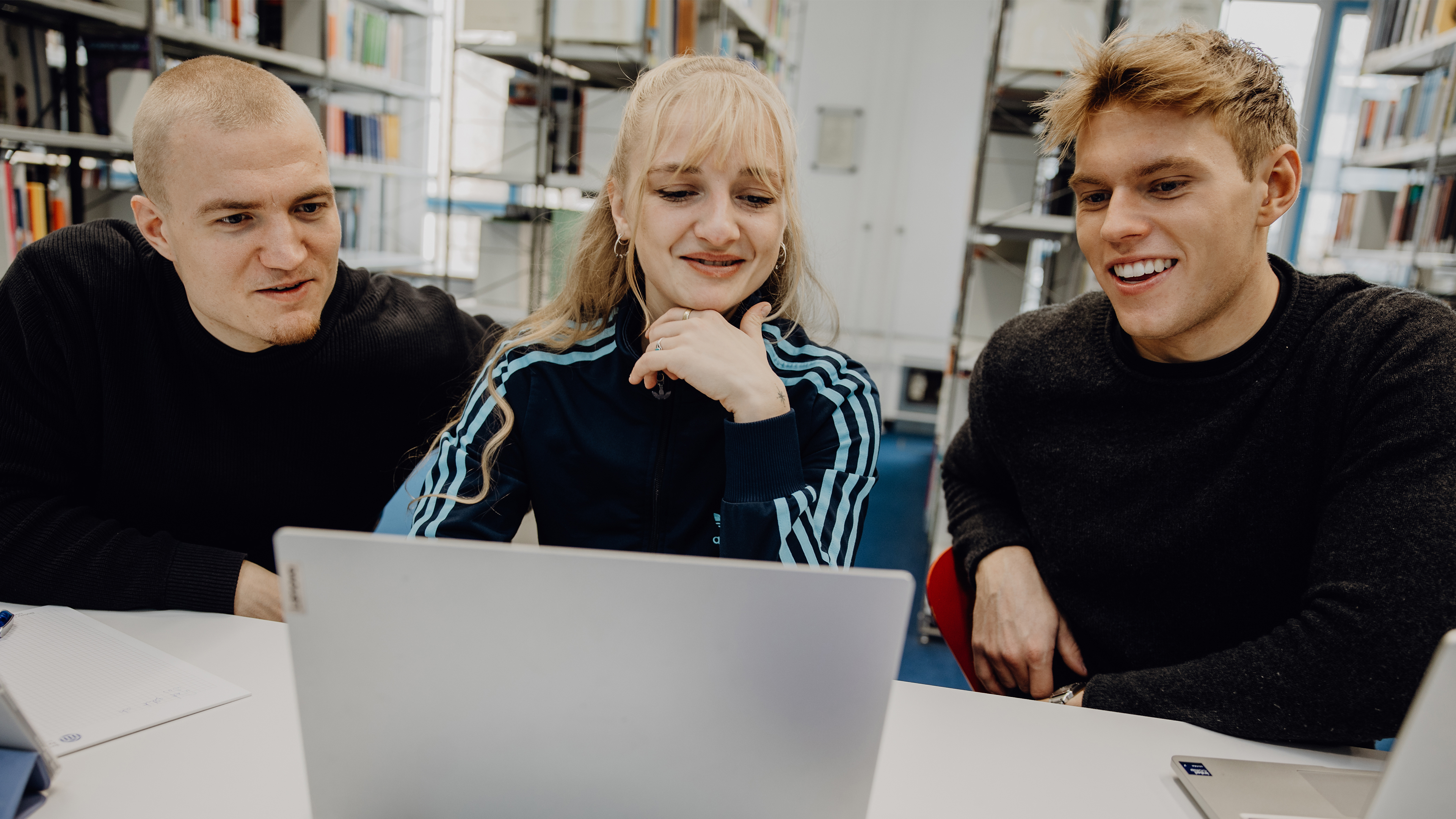 Drei Studierende sitzen vor einem Laptop in der Bibliothek der Deutschen Sporthochschule
