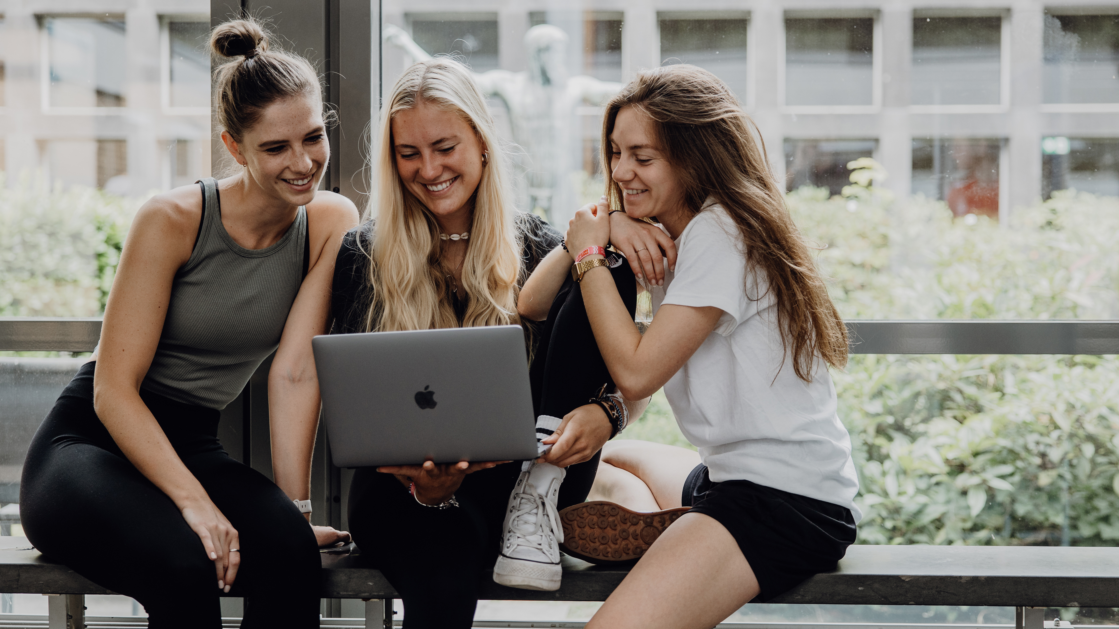 Dire Studierende sitzen mit einem Laptop im Foyer der Deutschen Sporthochschule
